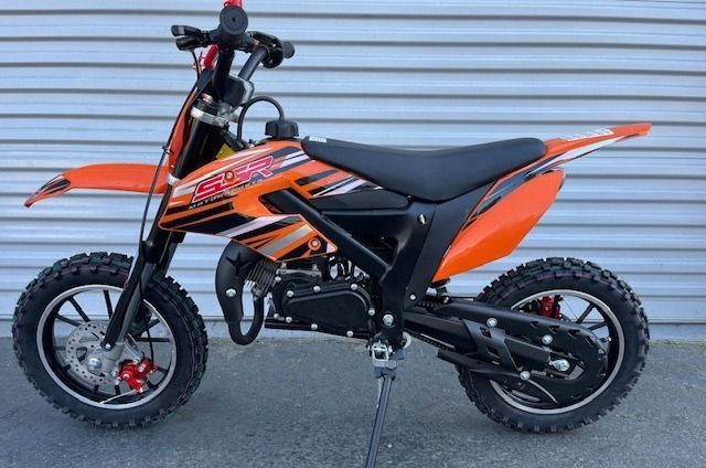 An orange dirt bike is parked in front of a wall