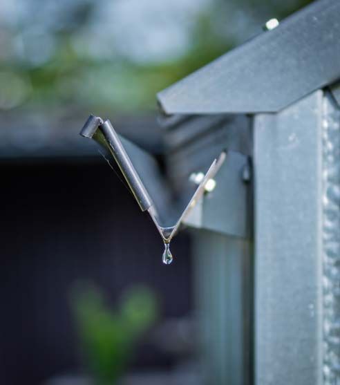 Rainwater dripping from a metal gutter, blurred background with green foliage.