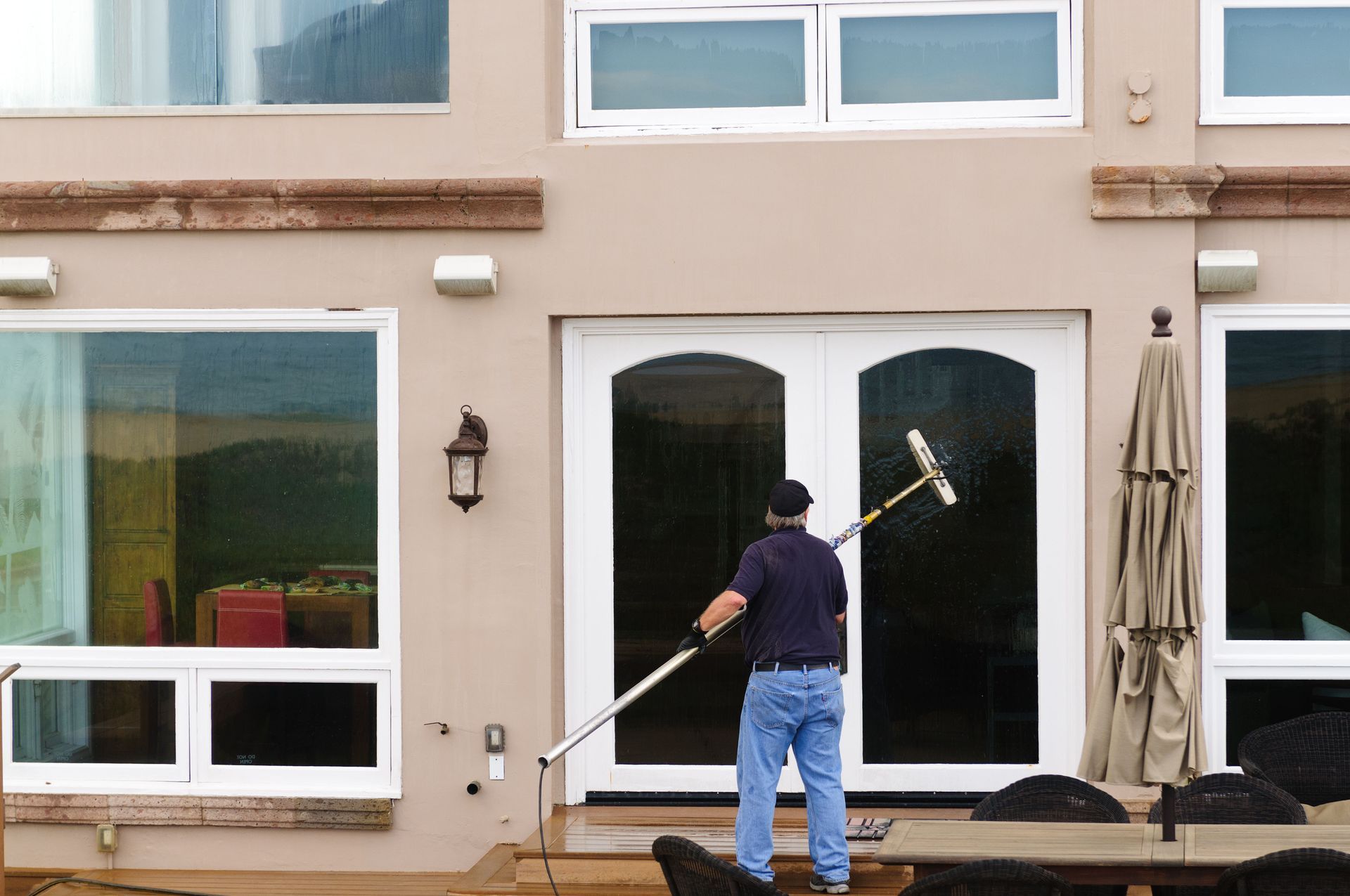 A worker cleans the exterior glass of a home's double doors using an extended pole and brush.