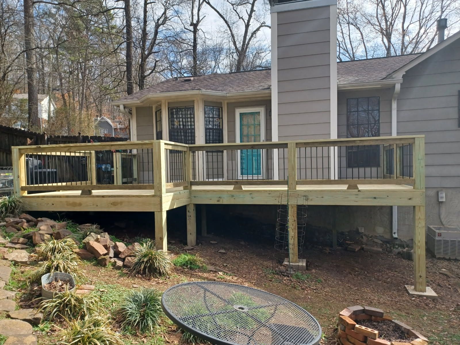 A new wooden deck attached to a house with black railings and a teal door.