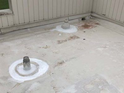 Flat white roof with vent pipes and white sealant around them; next to light beige siding.