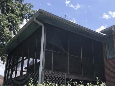 Screened-in porch with green trim, dark screens, and a small torn area. The sky is visible.