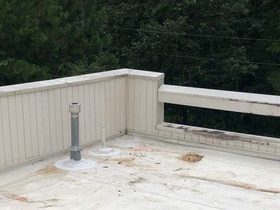 White flat roof with railing, a vent pipe, and surrounding trees.