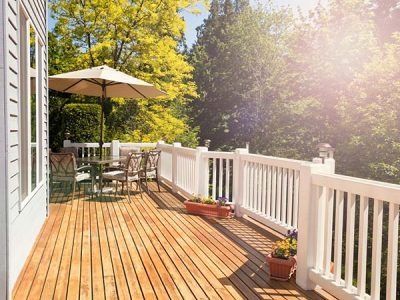 Wooden deck with white railing, table, umbrella, and chairs; sunny backyard setting.