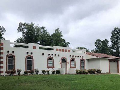 White stucco house with arched windows and red trim, under cloudy sky.
