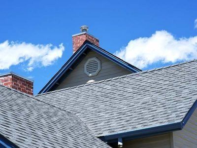 Gray shingle roofs, brick chimneys, and a tan house against a blue sky with clouds.