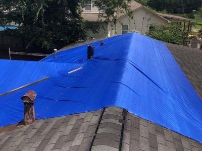 Blue tarp covering a residential roof, protecting damaged shingles from weather.