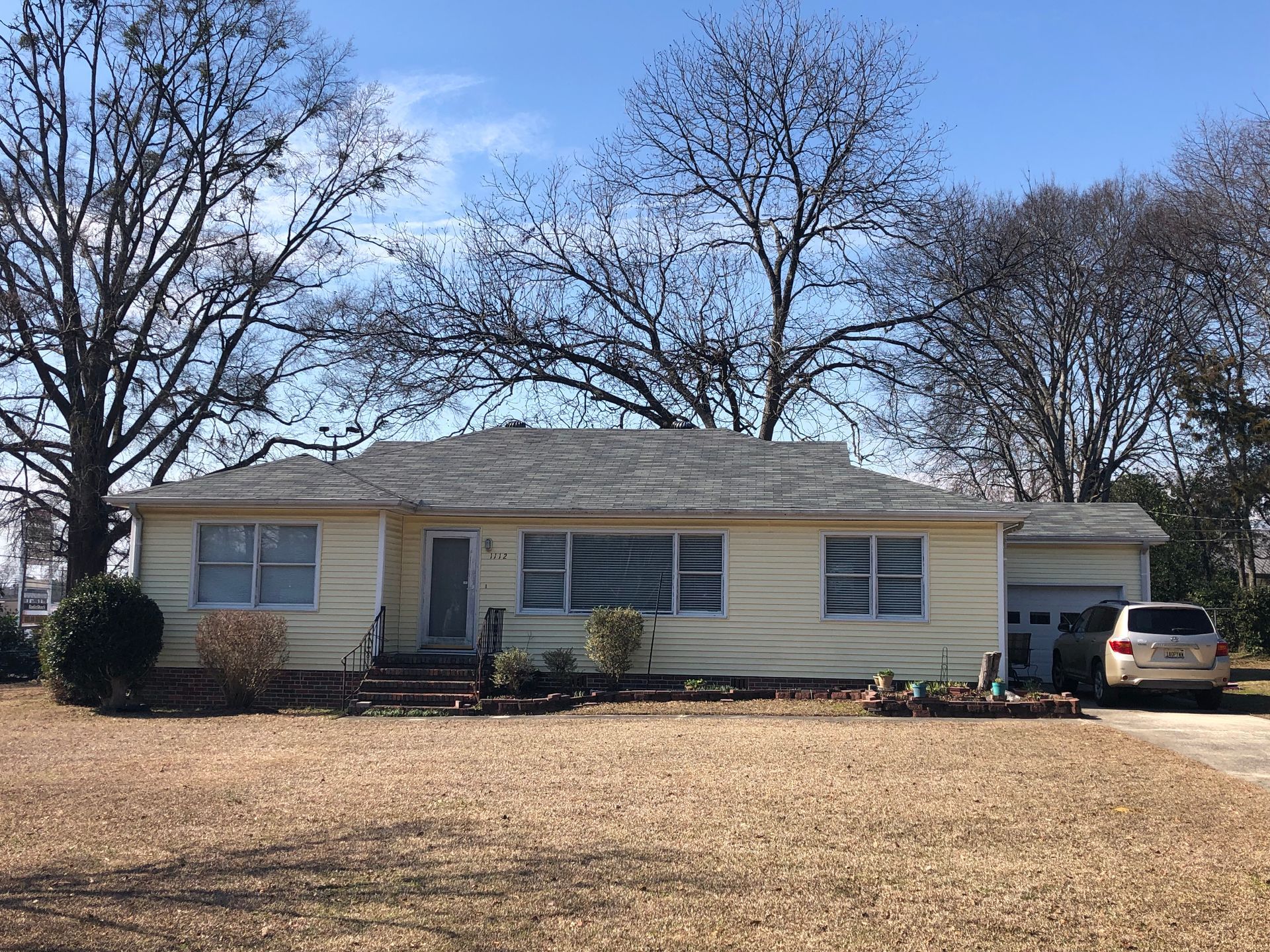 Yellow one-story house with a detached garage. Trees and a car are present in the daytime shot.