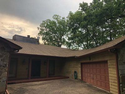 Tan house with brown roof, red trim, stone accents, and a red garage door under a cloudy sky.