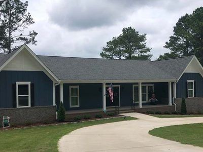 Blue house with a covered porch and American flag hanging; curved concrete driveway.