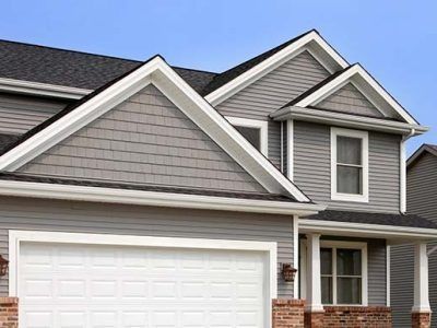 Gray house with white trim, a white garage door, and a brick foundation under a blue sky.