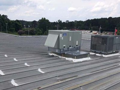 HVAC units on a metal roof, with a parking lot and trees in the background under a cloudy sky.