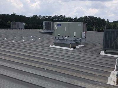Gray metal roof with HVAC units. Blue sky and trees in the background.