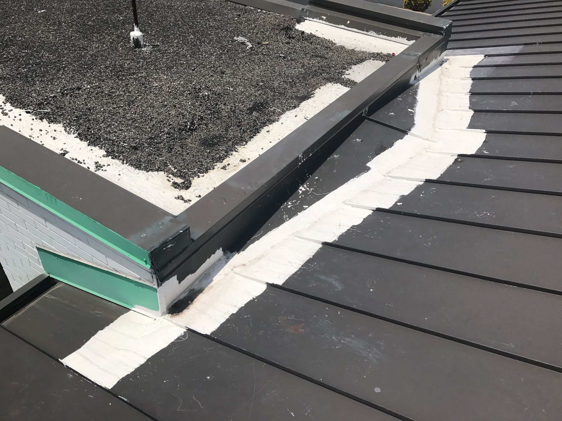 Dark roof with light sealant at the edges where it meets a flat, gravel-covered section.
