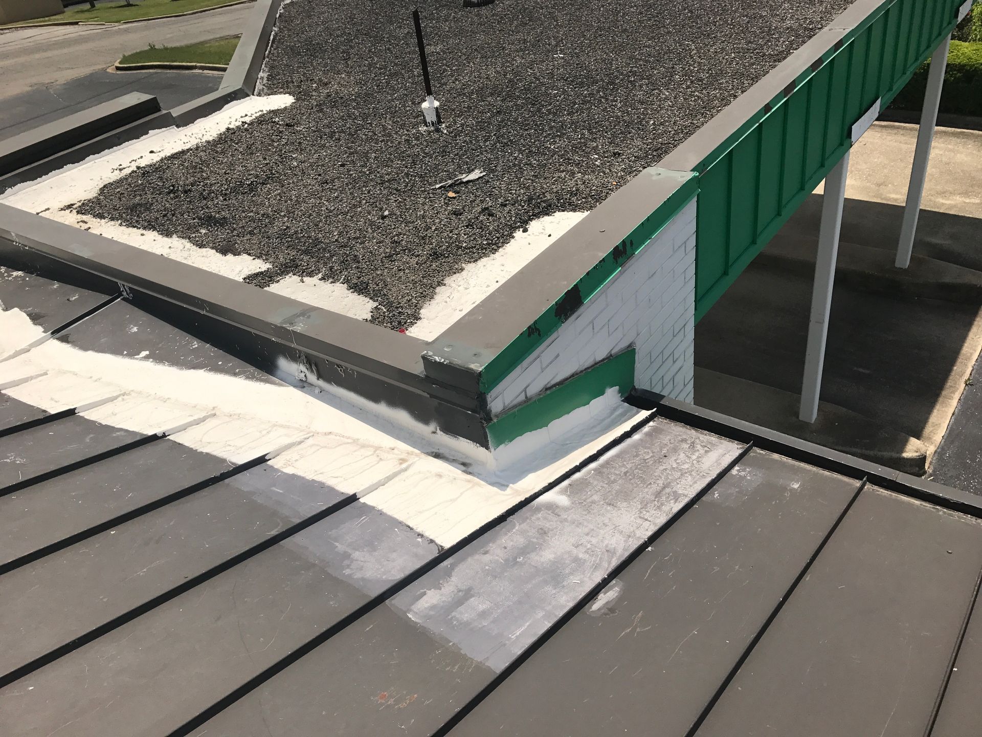 A flat roof with dark gray tiles and a gravel-covered section, bordered by green metal and white sealant.