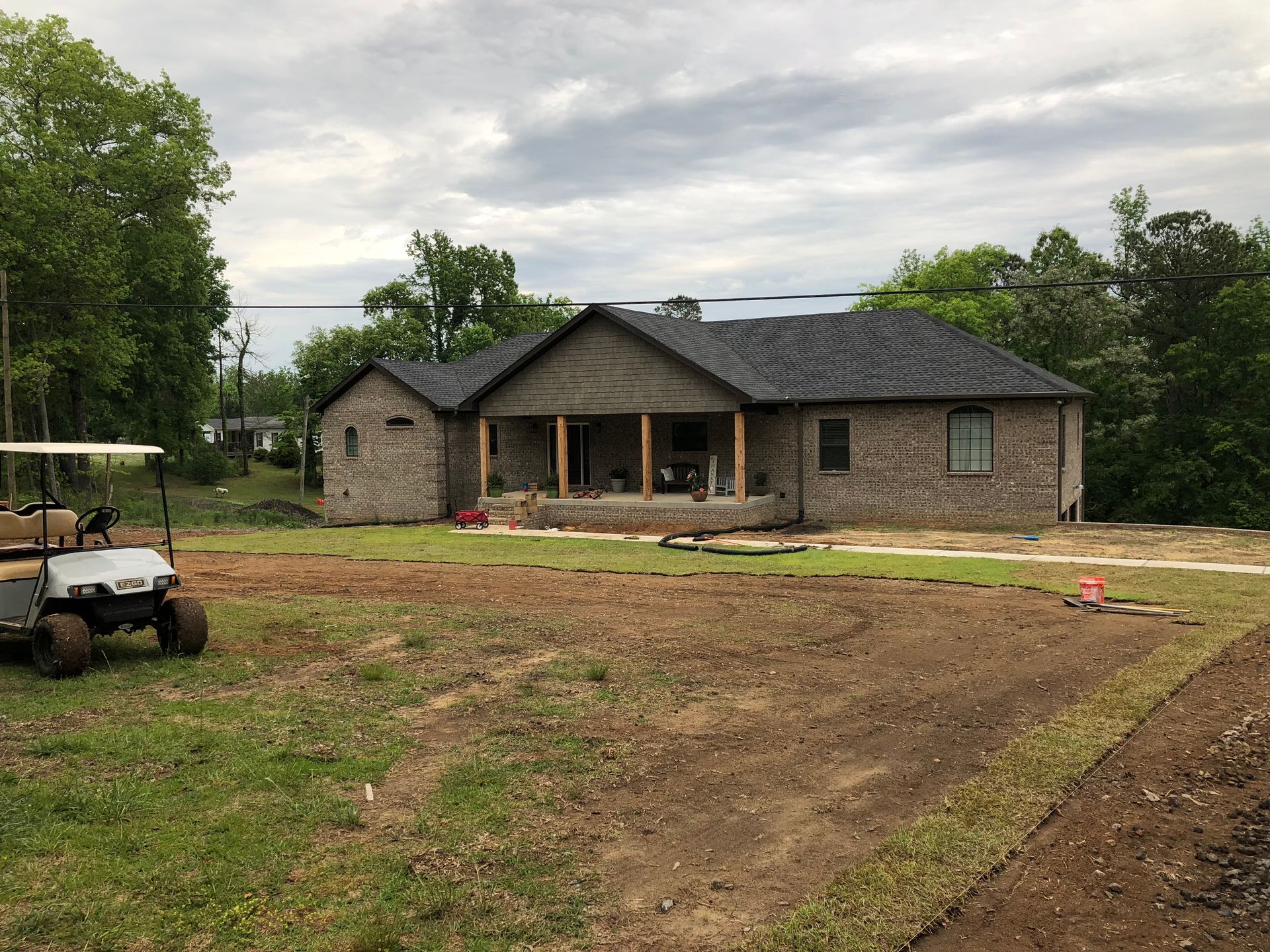 Brick house under construction with a porch and new roof. Lawn and golf cart in the foreground. Overcast sky.