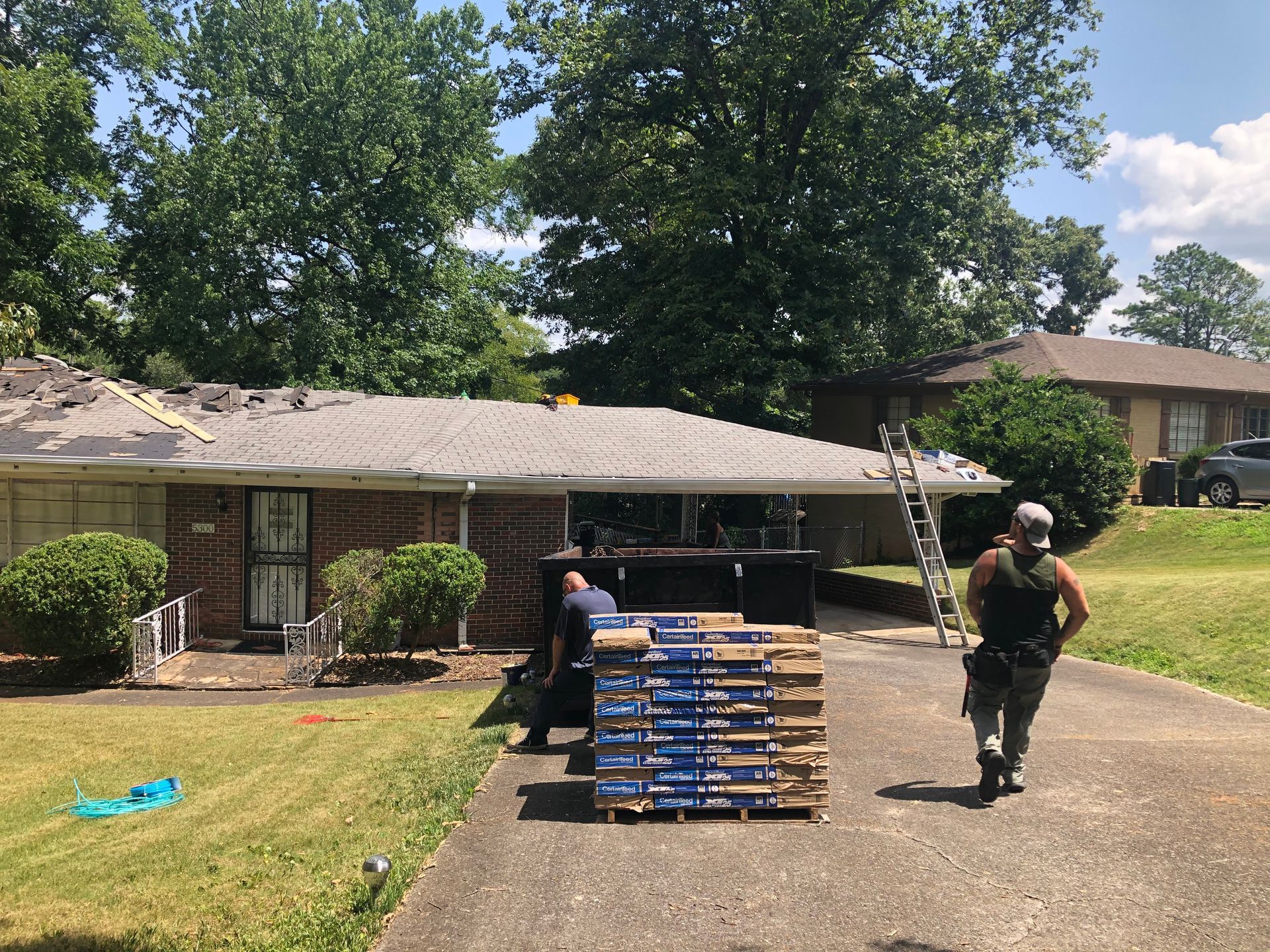 Roofers on a residential property. Two men load shingles onto the roof. One walks toward a pallet.