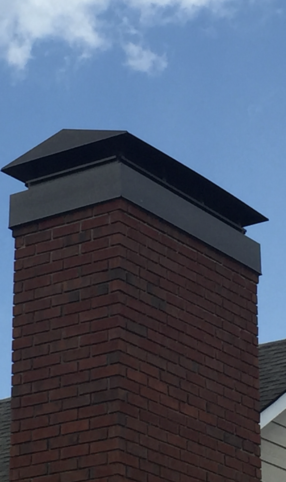 Brick chimney with a dark metal cap against a blue sky.