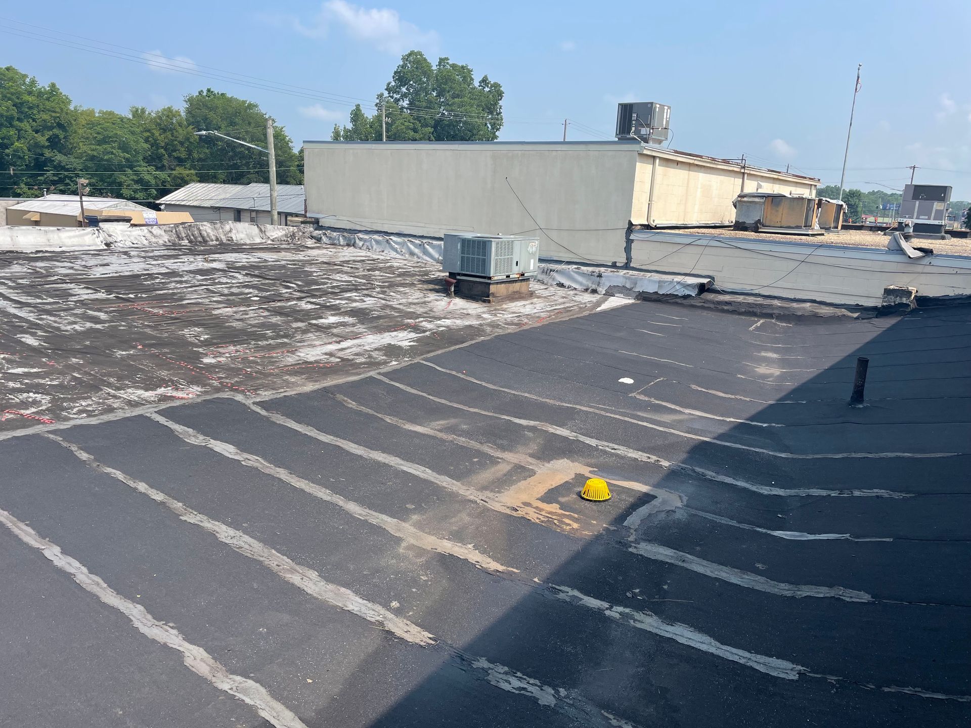 Black asphalt roof with a yellow hardhat and air conditioning units. Industrial buildings in background.