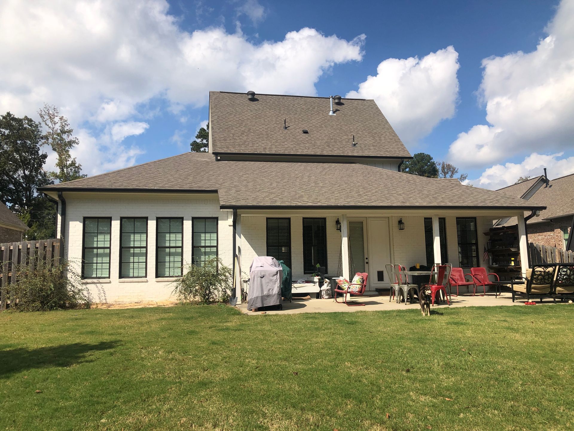 Rear view of a white house with a brown roof and a grassy lawn under a partly cloudy sky.
