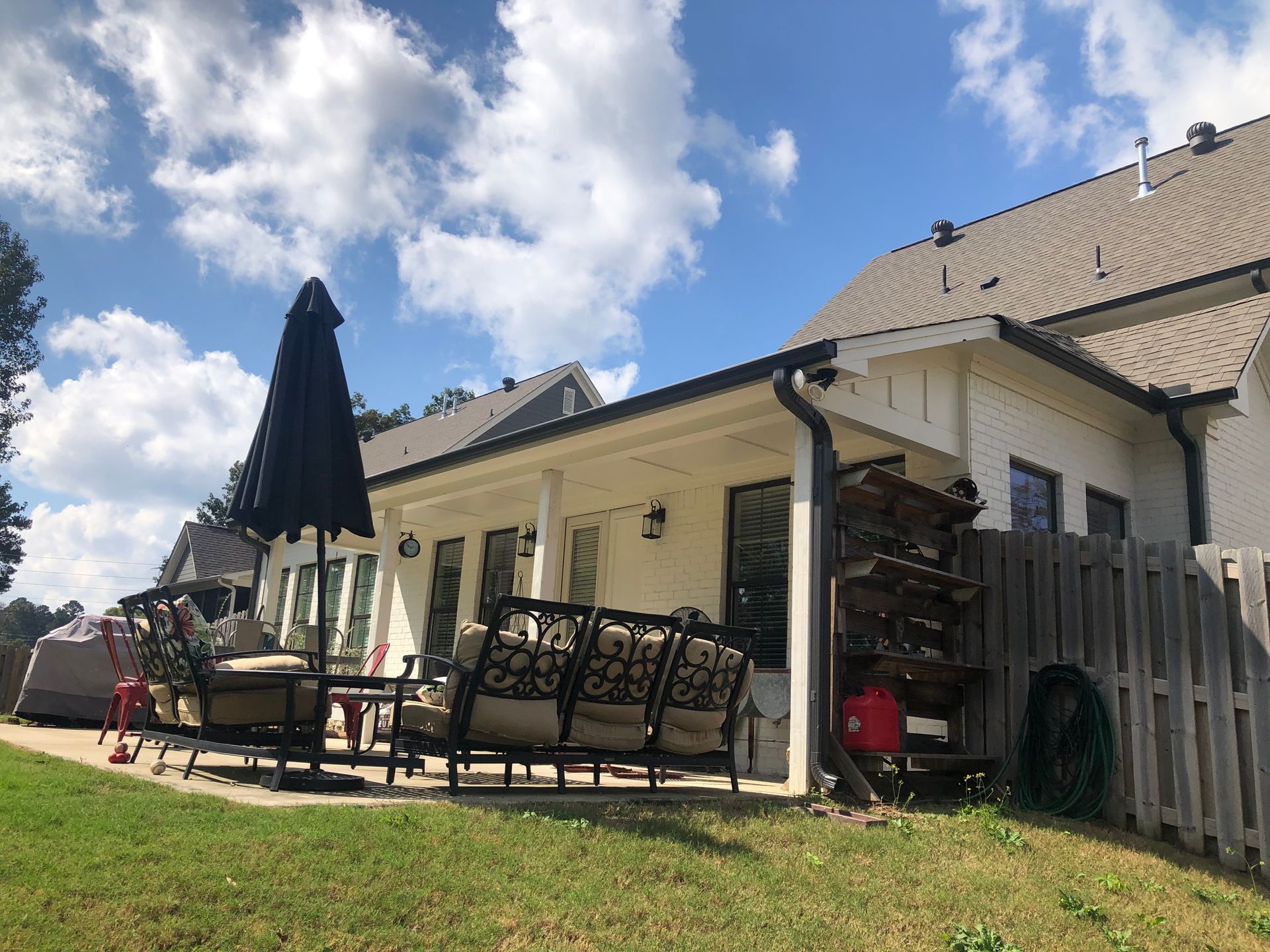 Backyard patio with outdoor furniture, umbrella, and white house with a blue sky.