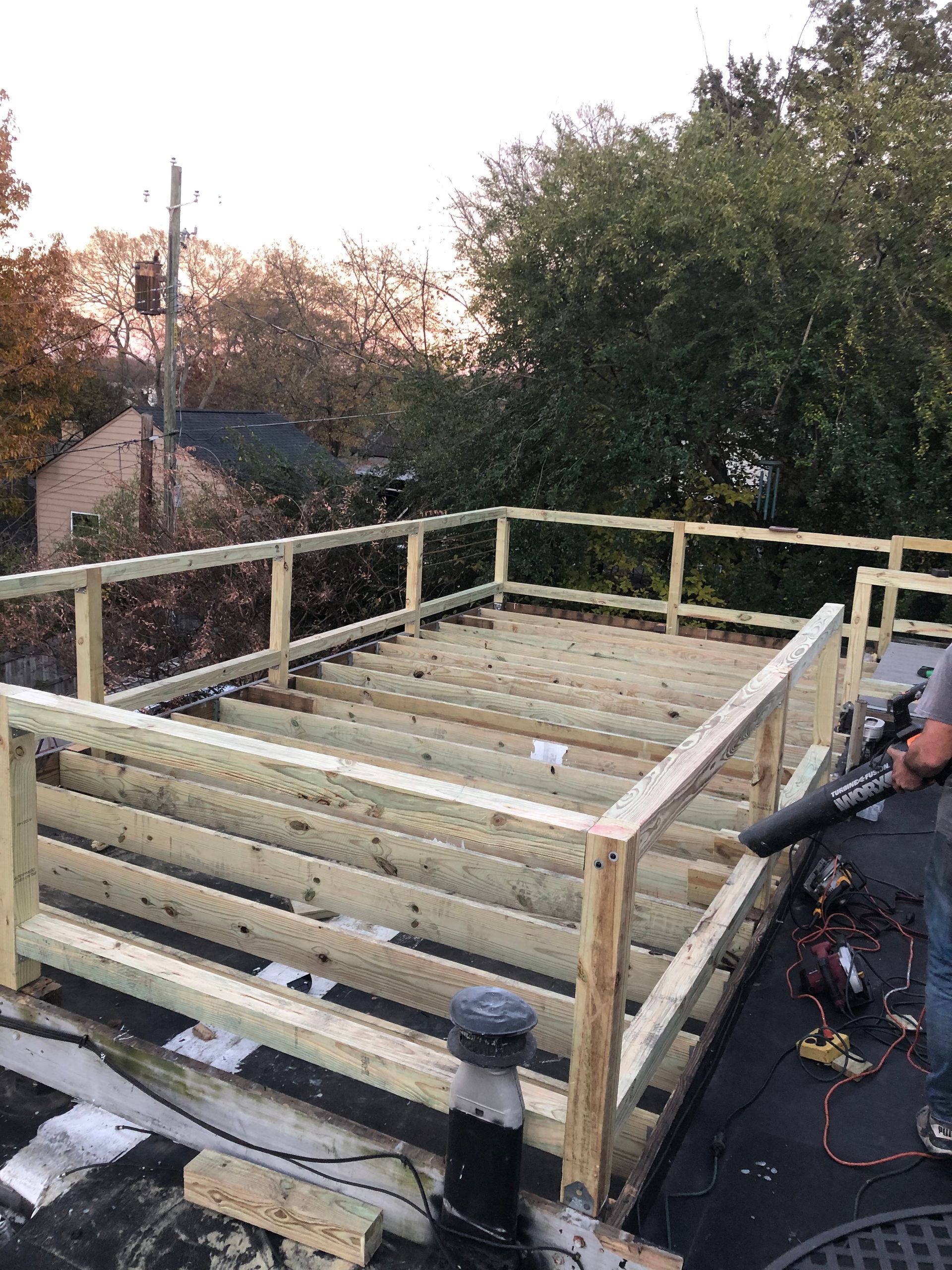 Wooden deck frame on a rooftop, with a person operating a leaf blower.