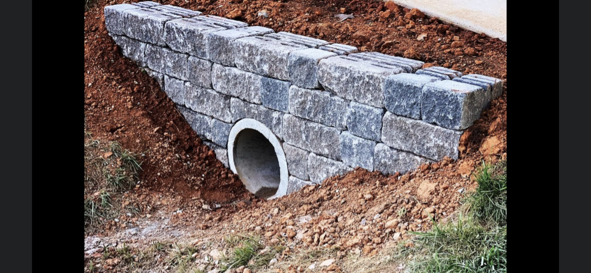 Stone retaining wall with culvert pipe outlet.