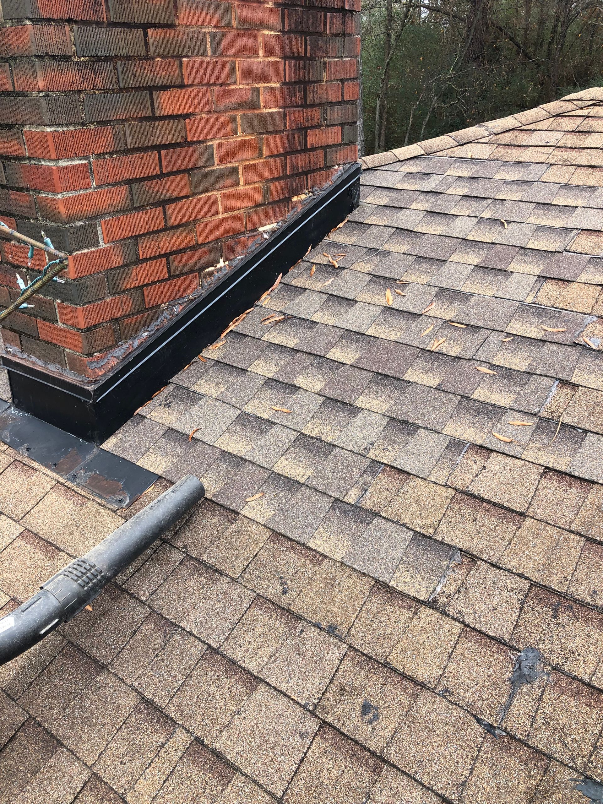 Brick chimney on a shingled roof with black flashing. A gutter is in the foreground.