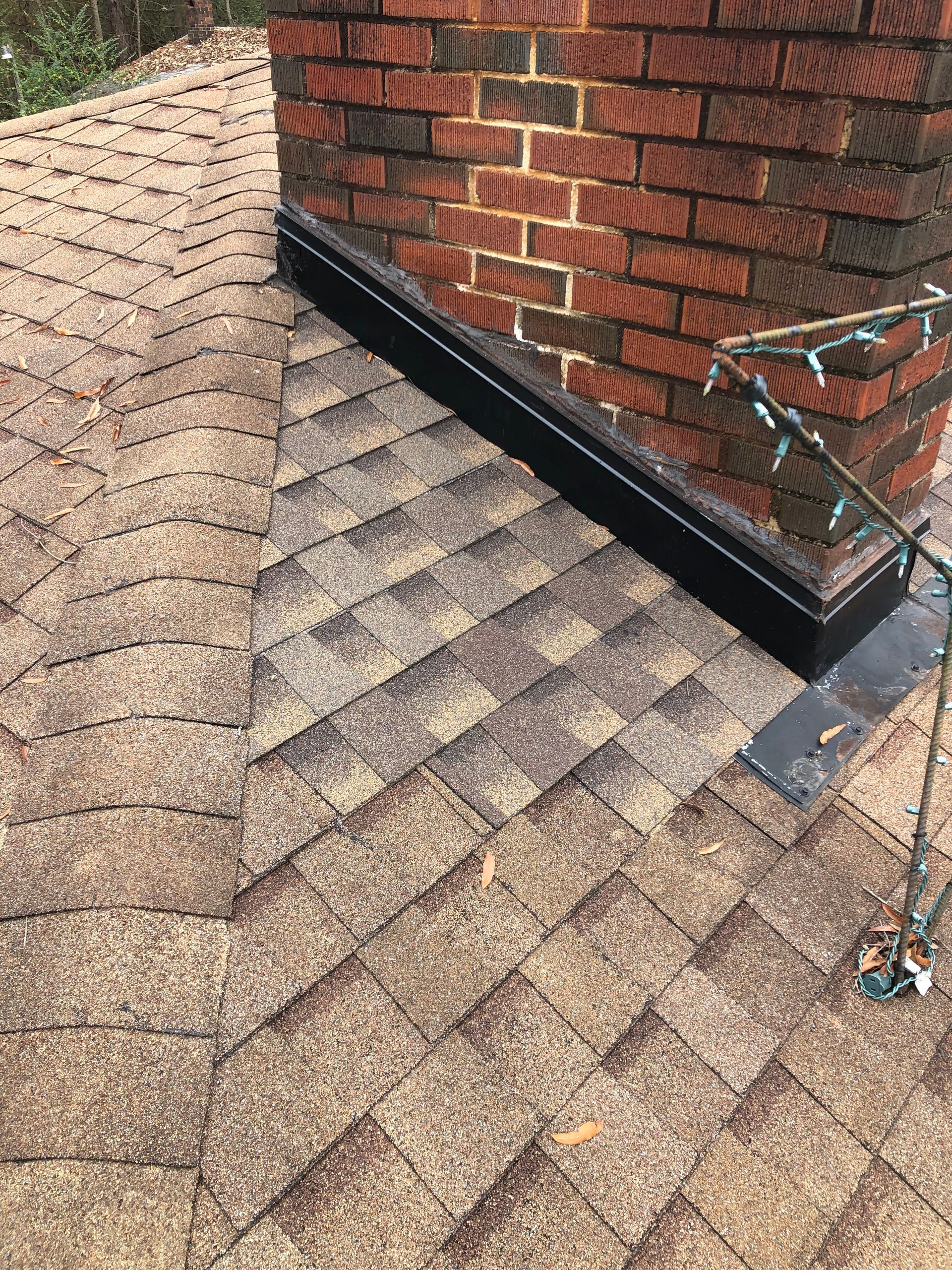 Brown shingle roof with a brick chimney and black flashing.