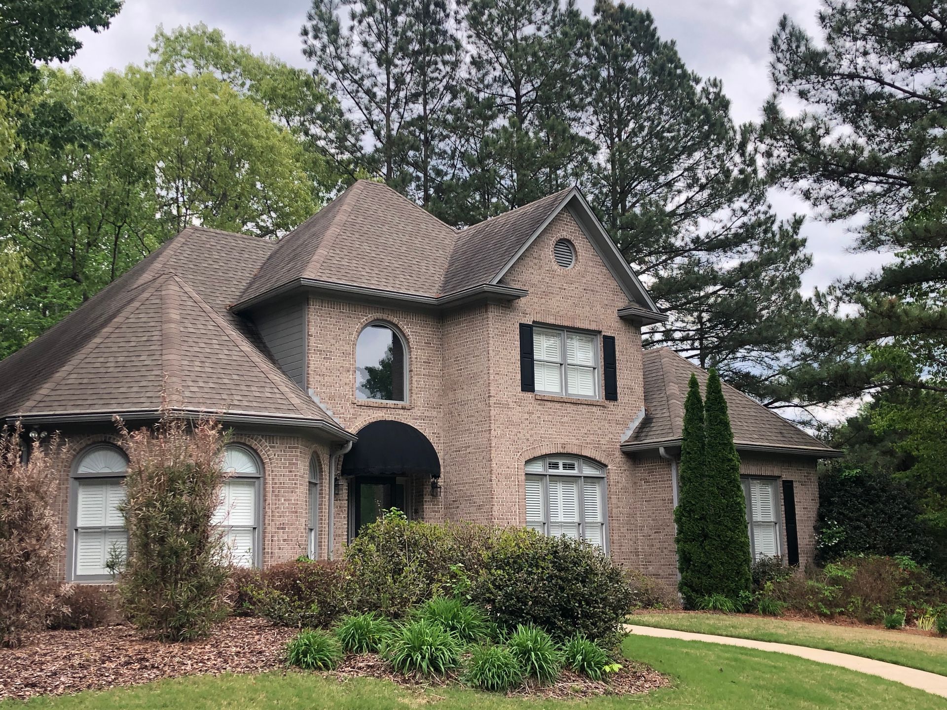 Brick house with arched windows, black shutters, and a dark roof; green lawn and trees in the background.
