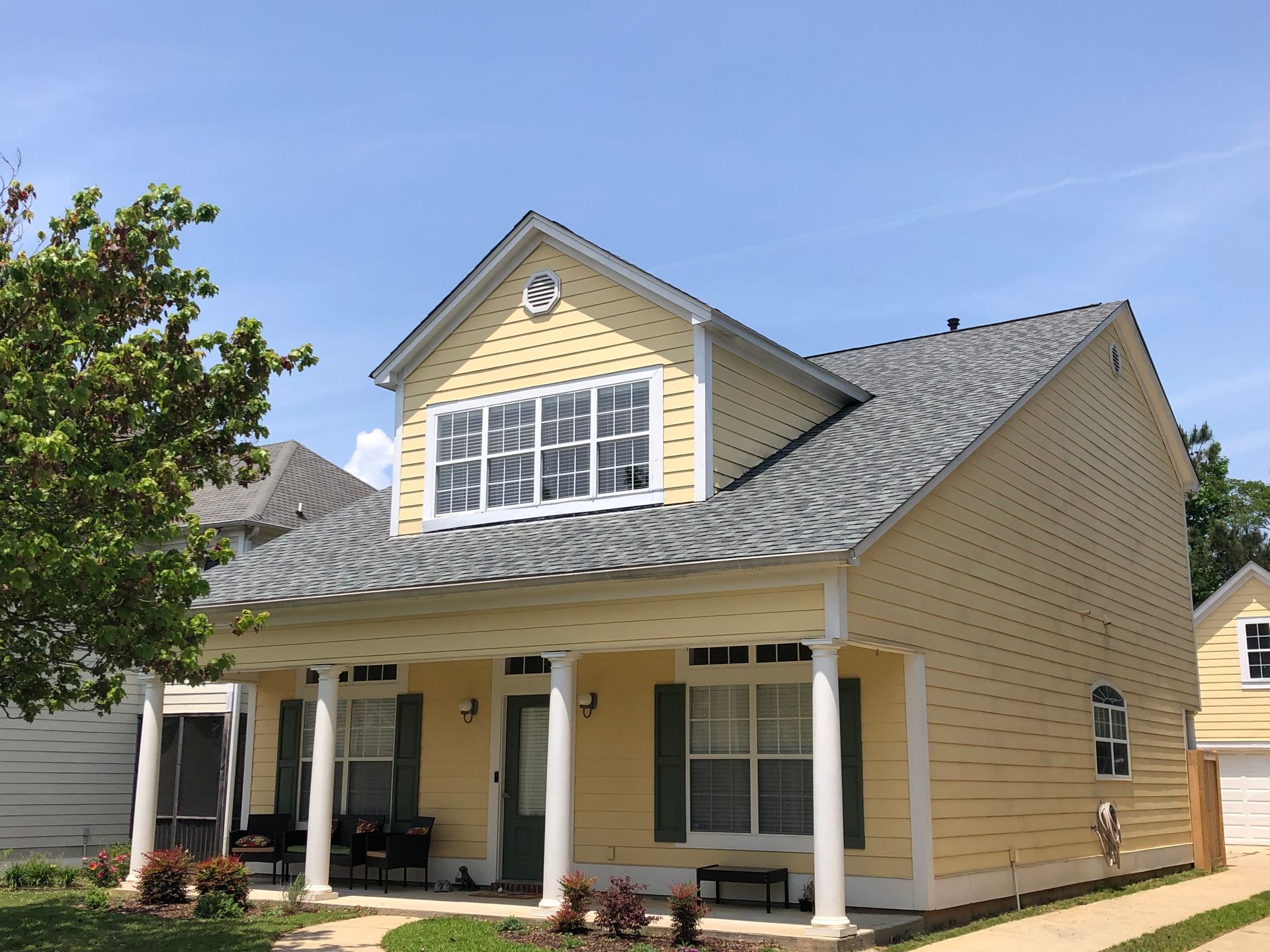 Yellow two-story house with porch, white columns, gray roof, and green shutters under a blue sky.