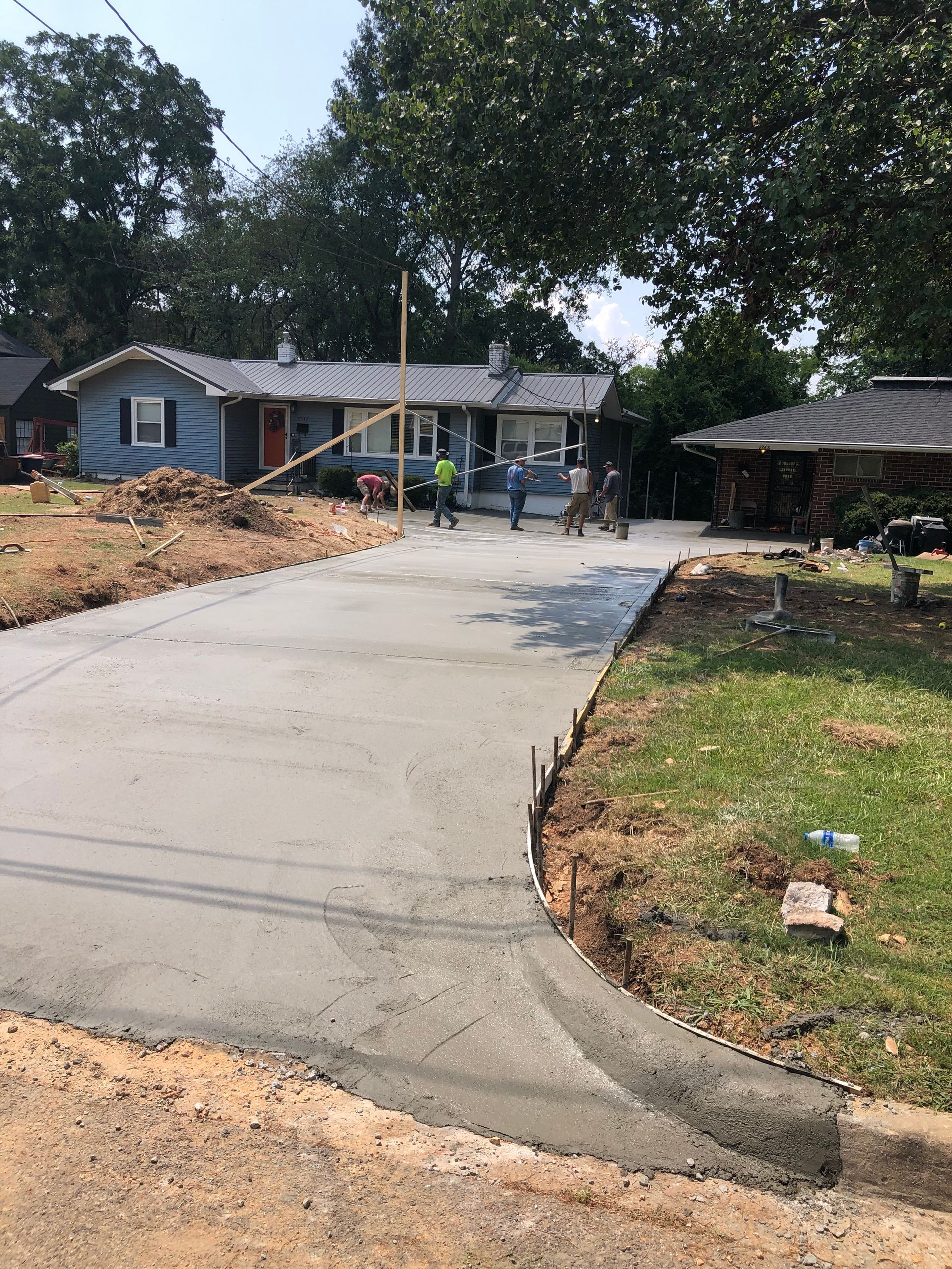 Workers pouring fresh concrete for a driveway in front of a blue house.
