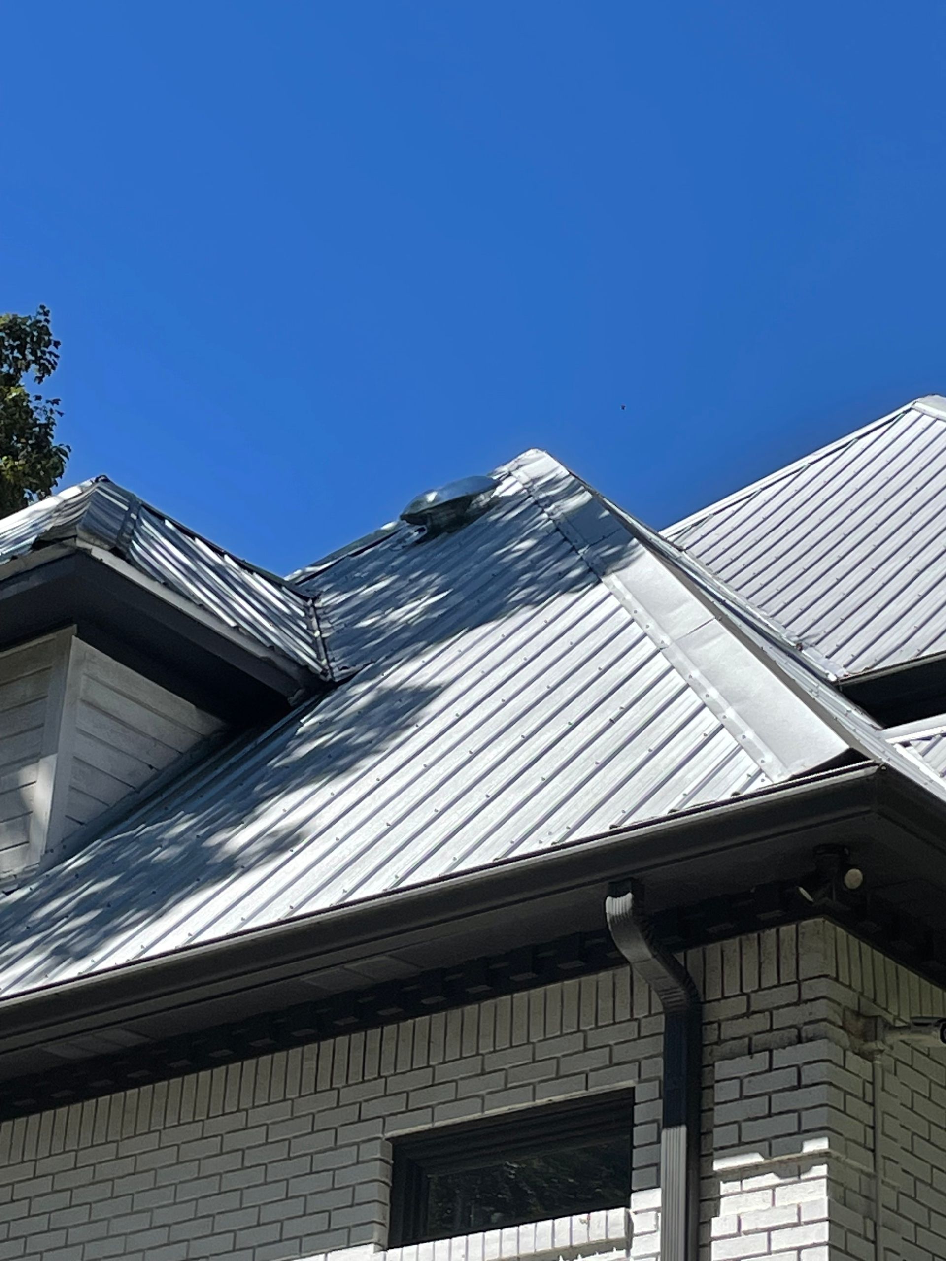 White metal roof on a brick house with black gutters and a clear blue sky.