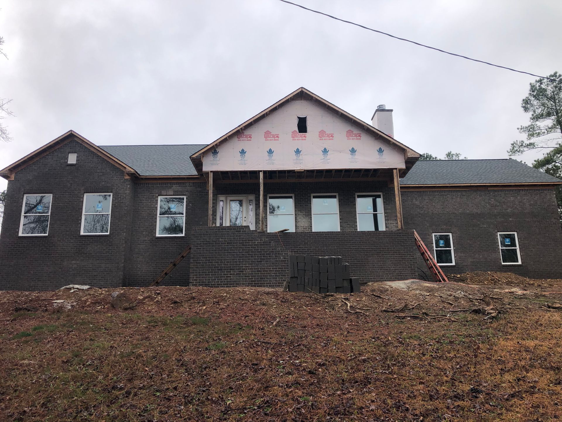 House under construction with brick exterior and unfinished roof, cloudy day.
