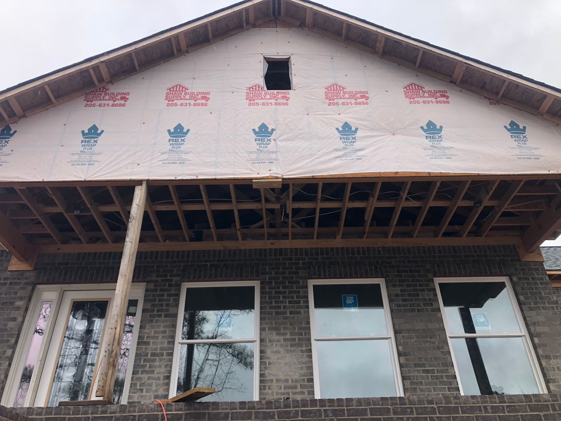 Exterior of a house under construction; brick, windows, wood framing, and sheathing are visible.