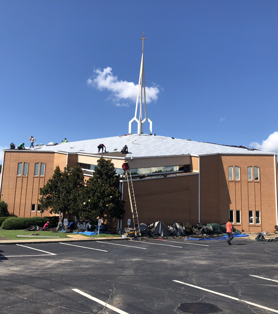 Church roof being repaired; workers on the roof, ladder in use, building is brick.