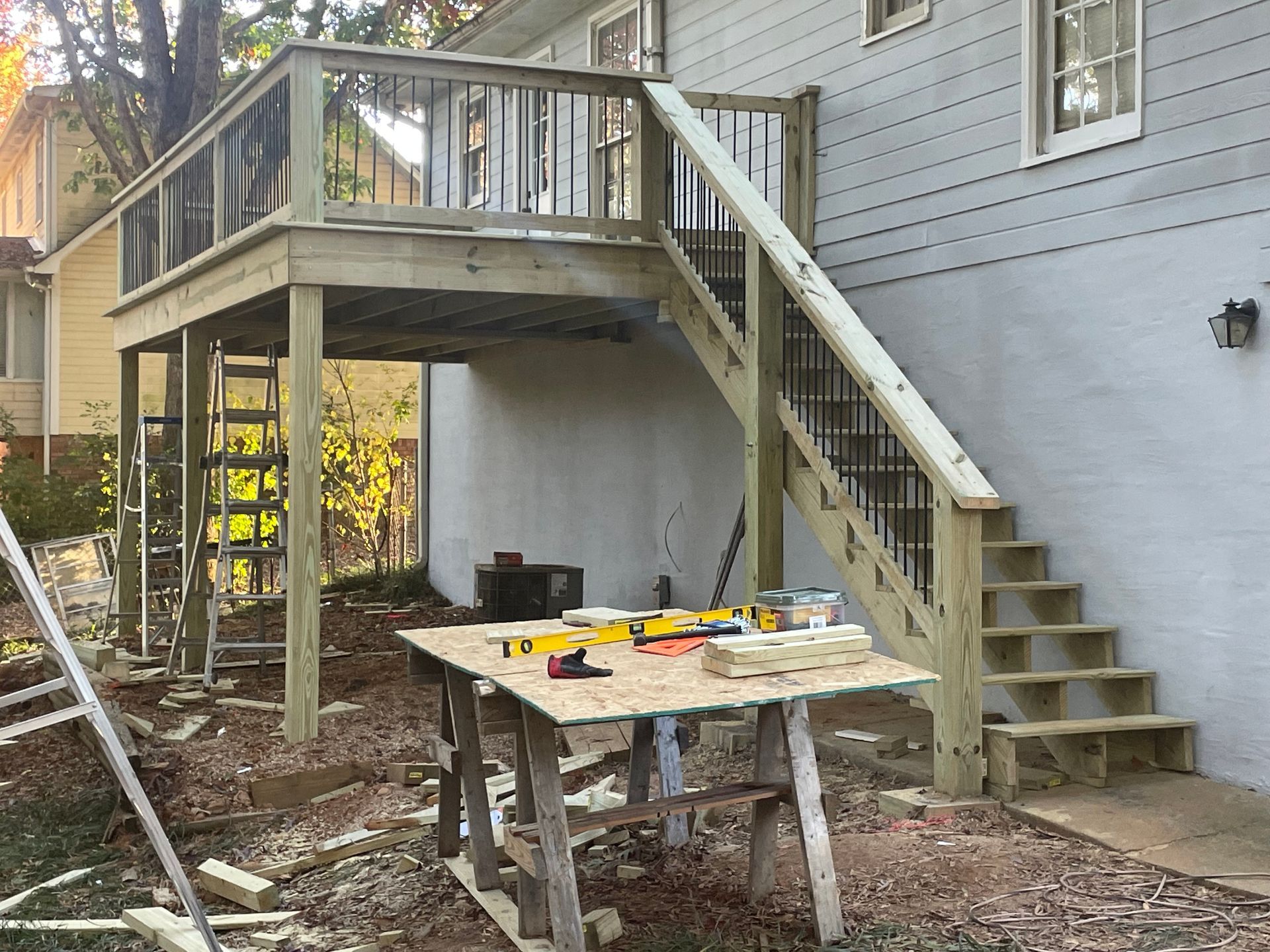 A wooden deck under construction; stairs, railing, tools, and a sawhorse are visible outdoors.