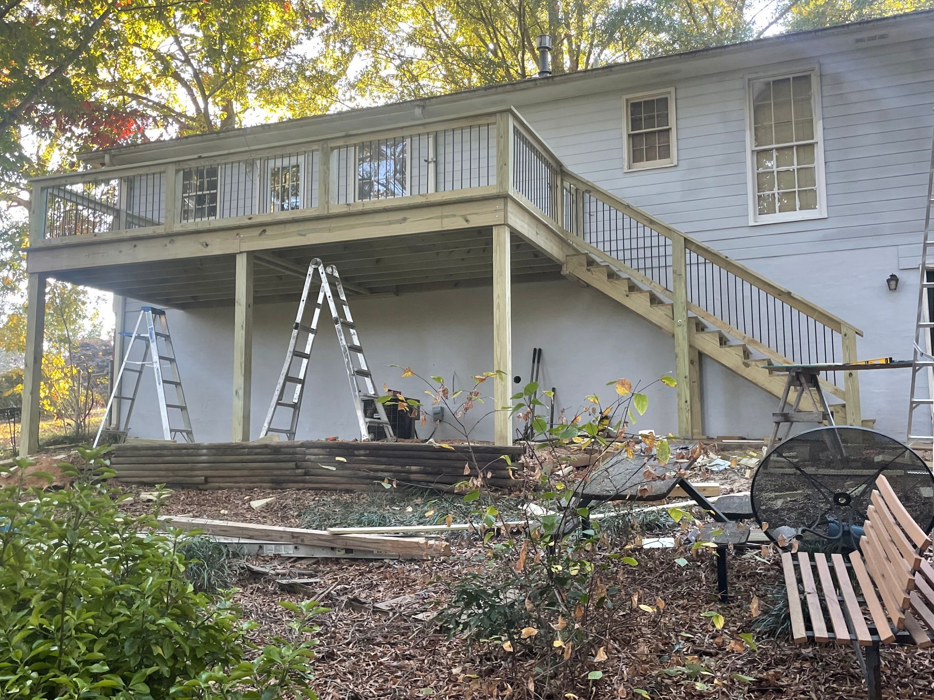 Two-story wooden deck under construction; ladders and tools visible. Grey house with white windows.