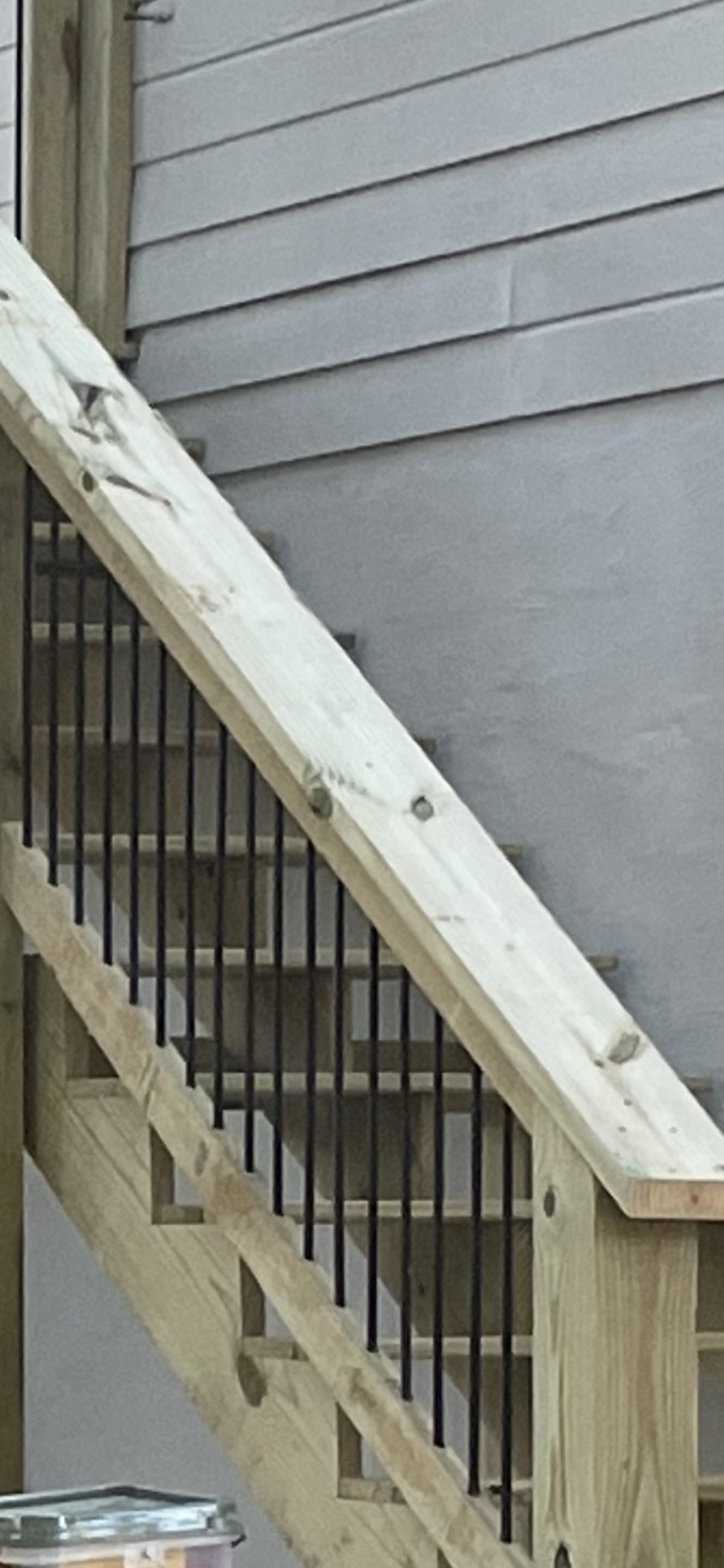 Wooden outdoor staircase with black metal railings against gray siding.