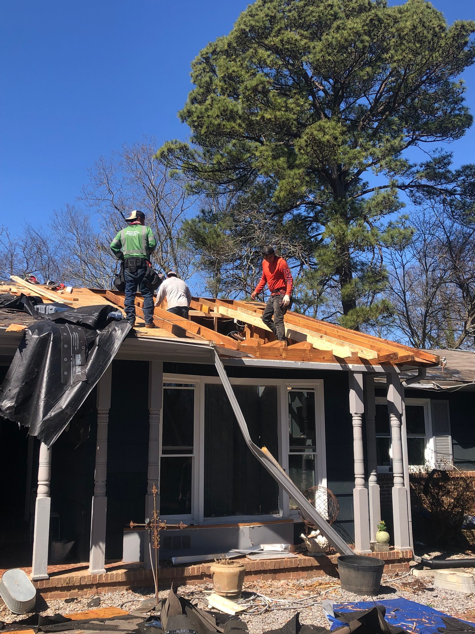 Men working on roof of damaged house on a sunny day.