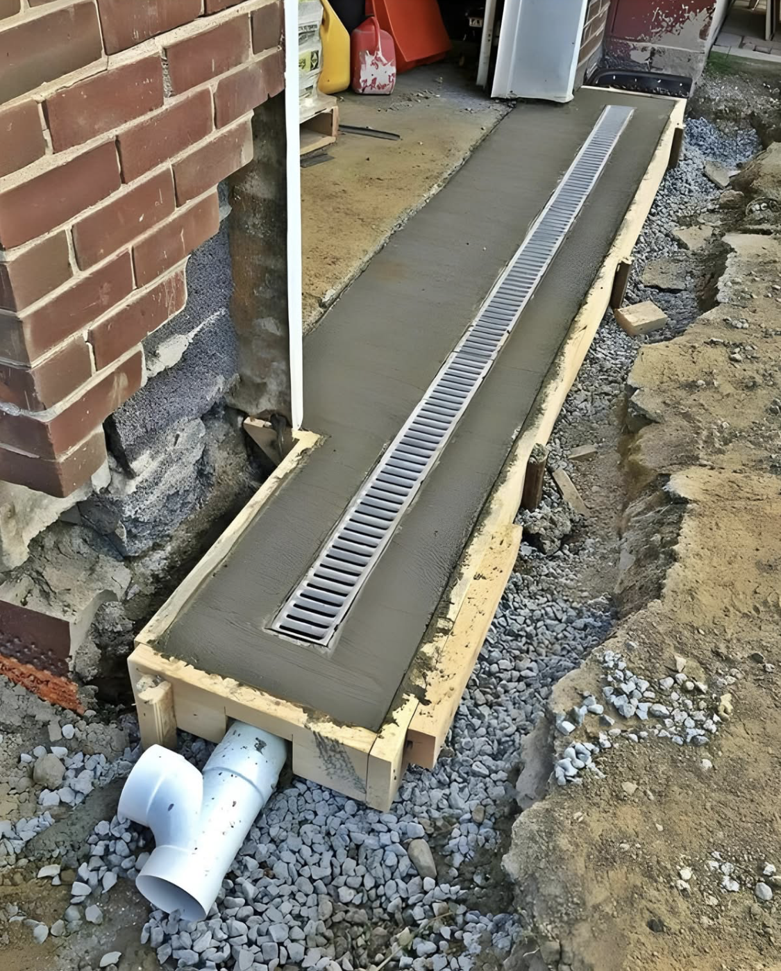Construction of a concrete drainage channel next to a brick building.