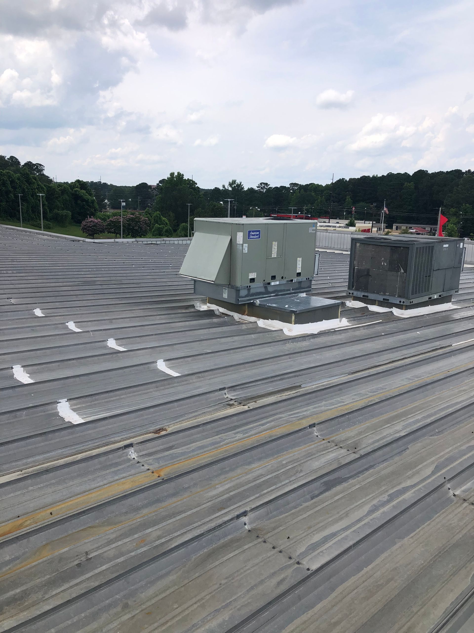 Rooftop with two HVAC units and a corrugated metal surface, cloudy sky backdrop.