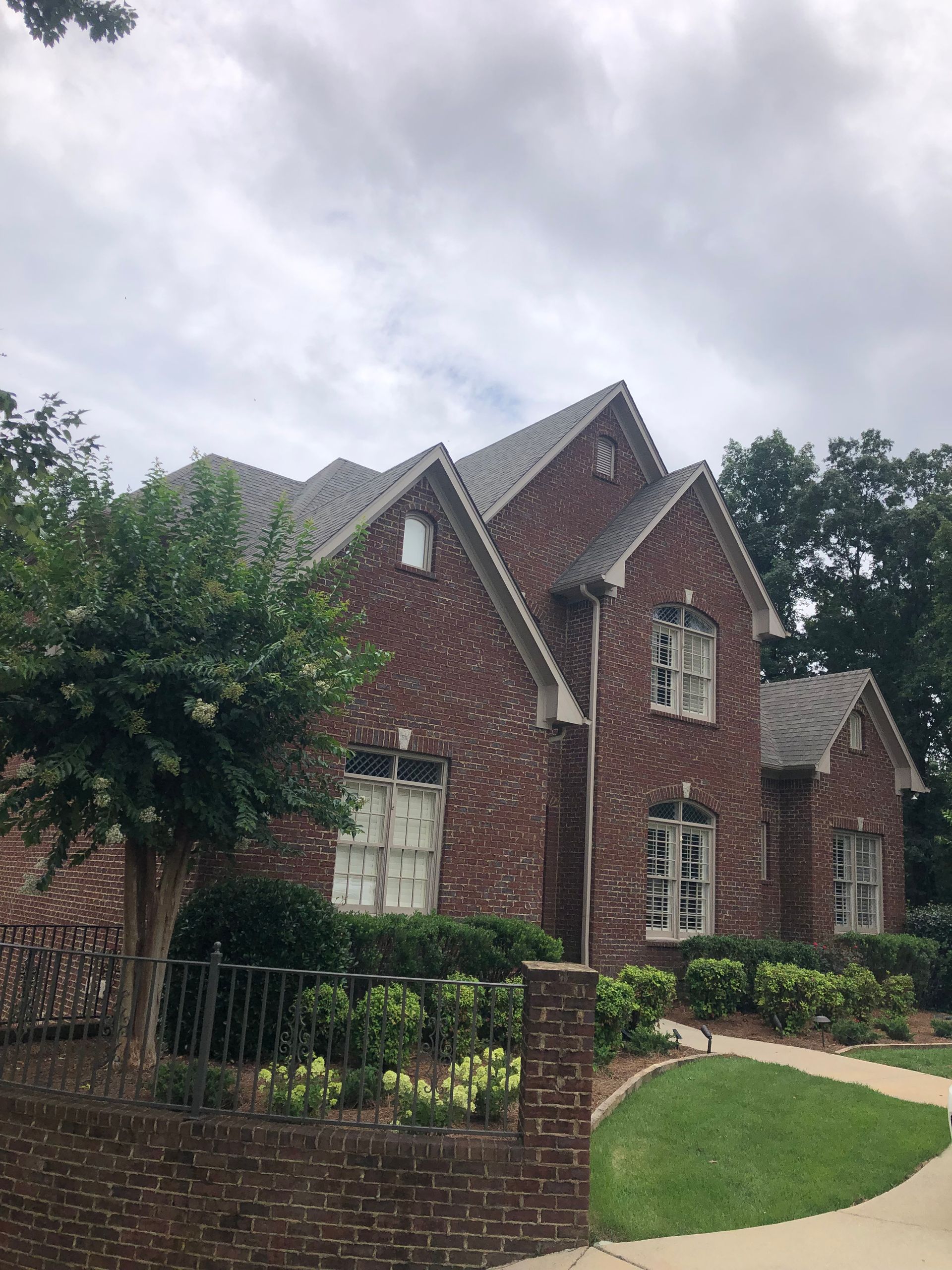 Red brick house with multiple gables under a cloudy sky, surrounded by greenery.