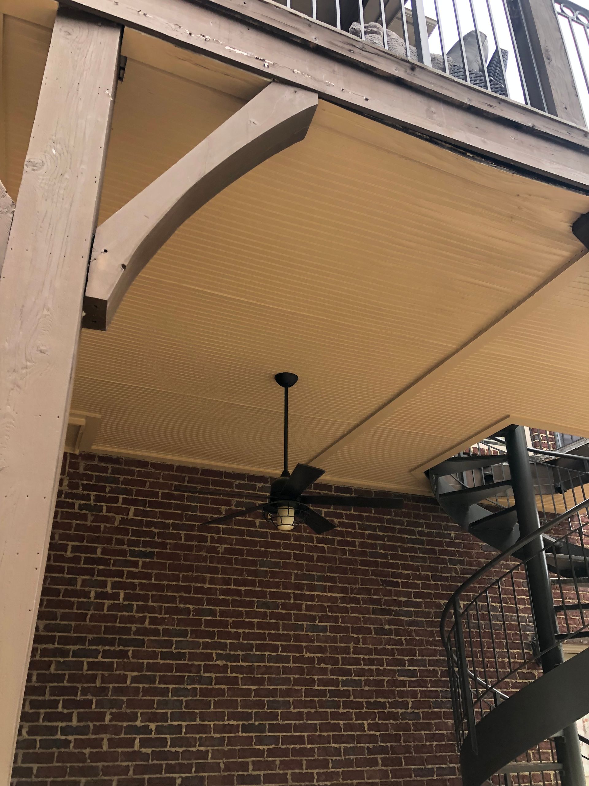 Brick wall, ceiling with fan, and spiral staircase. Overhang with arched supports, light brown and tan colors.