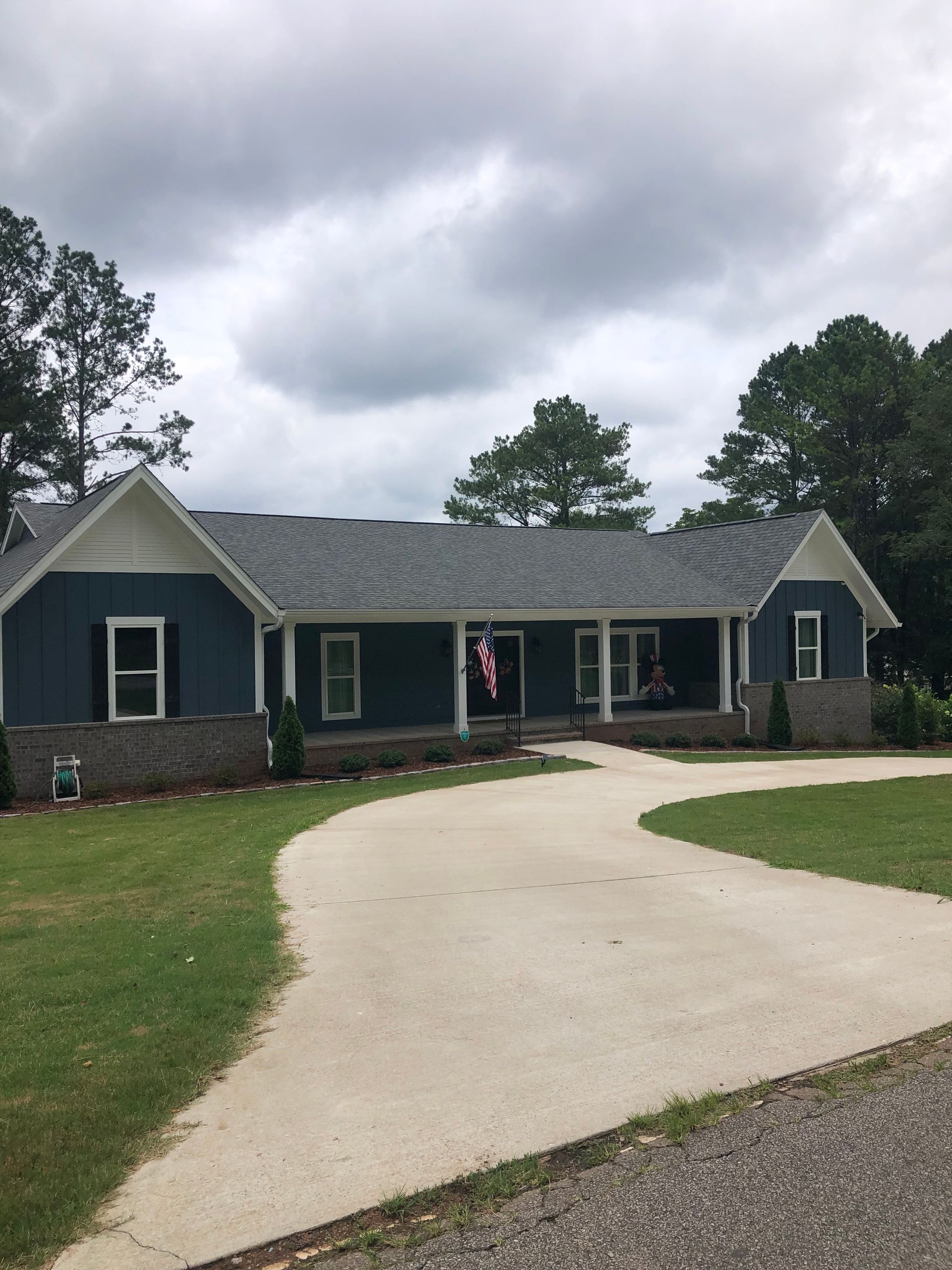 Blue house with white trim, porch, and long driveway on a cloudy day.