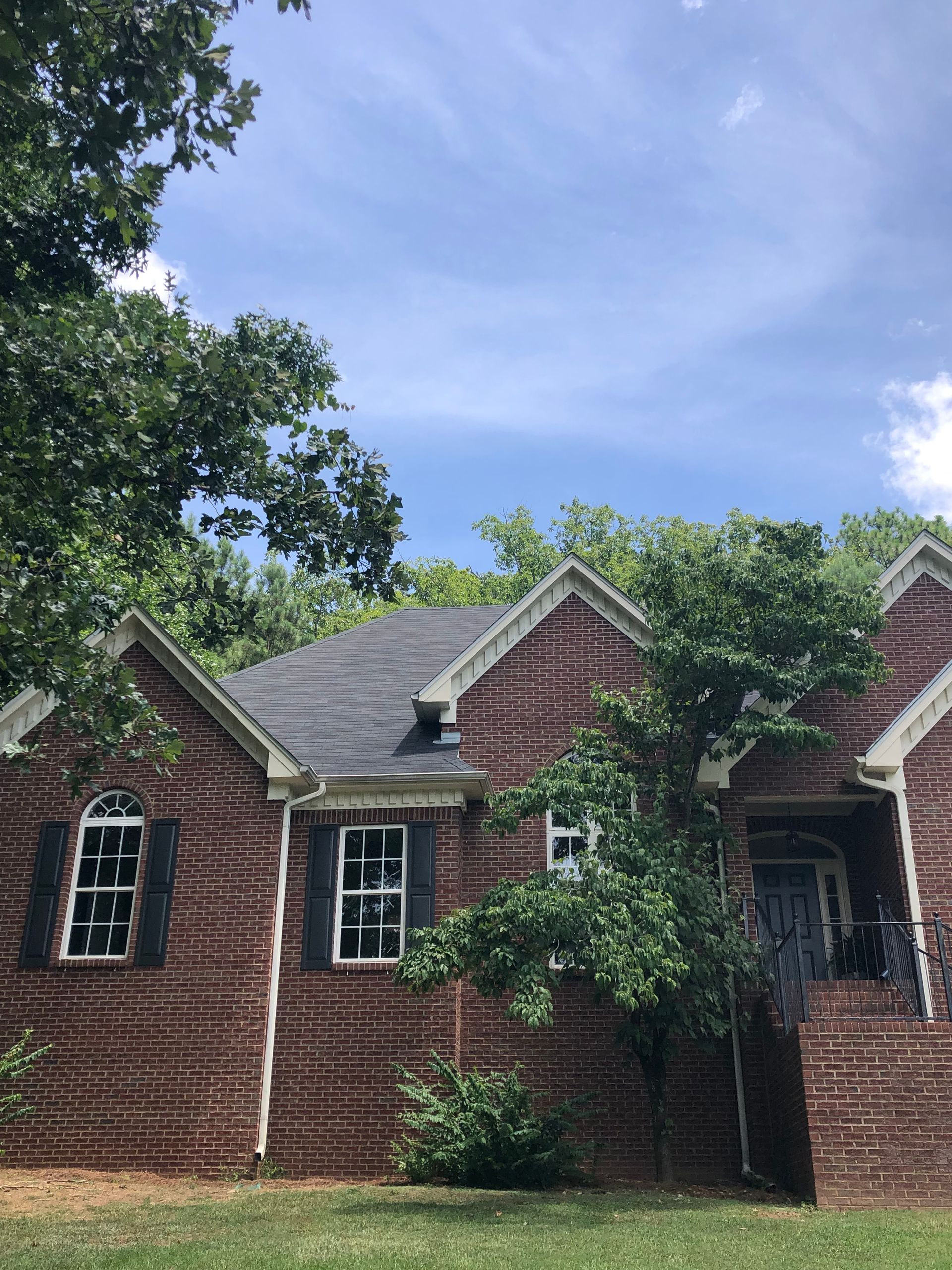 Brick house with black roof, trees, and blue sky.