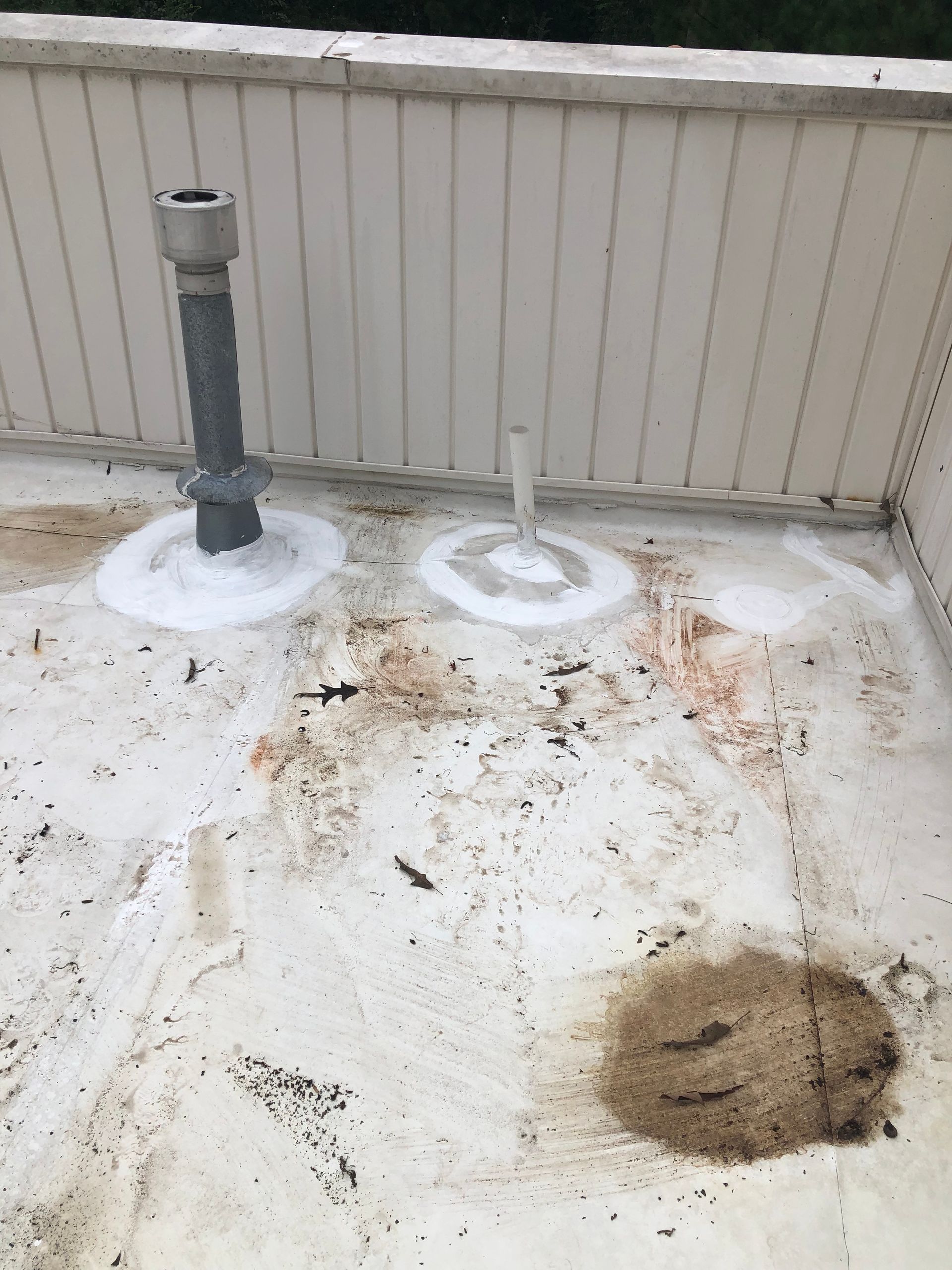Flat rooftop with vent pipes and stains. White surface with dirt and possible water damage.