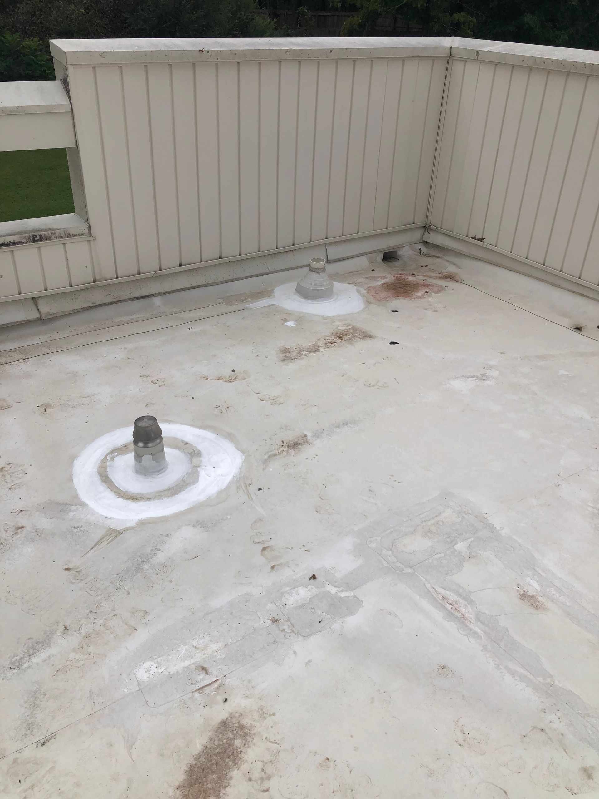 White flat roof with three pipe protrusions, light discoloration, and a beige fence.