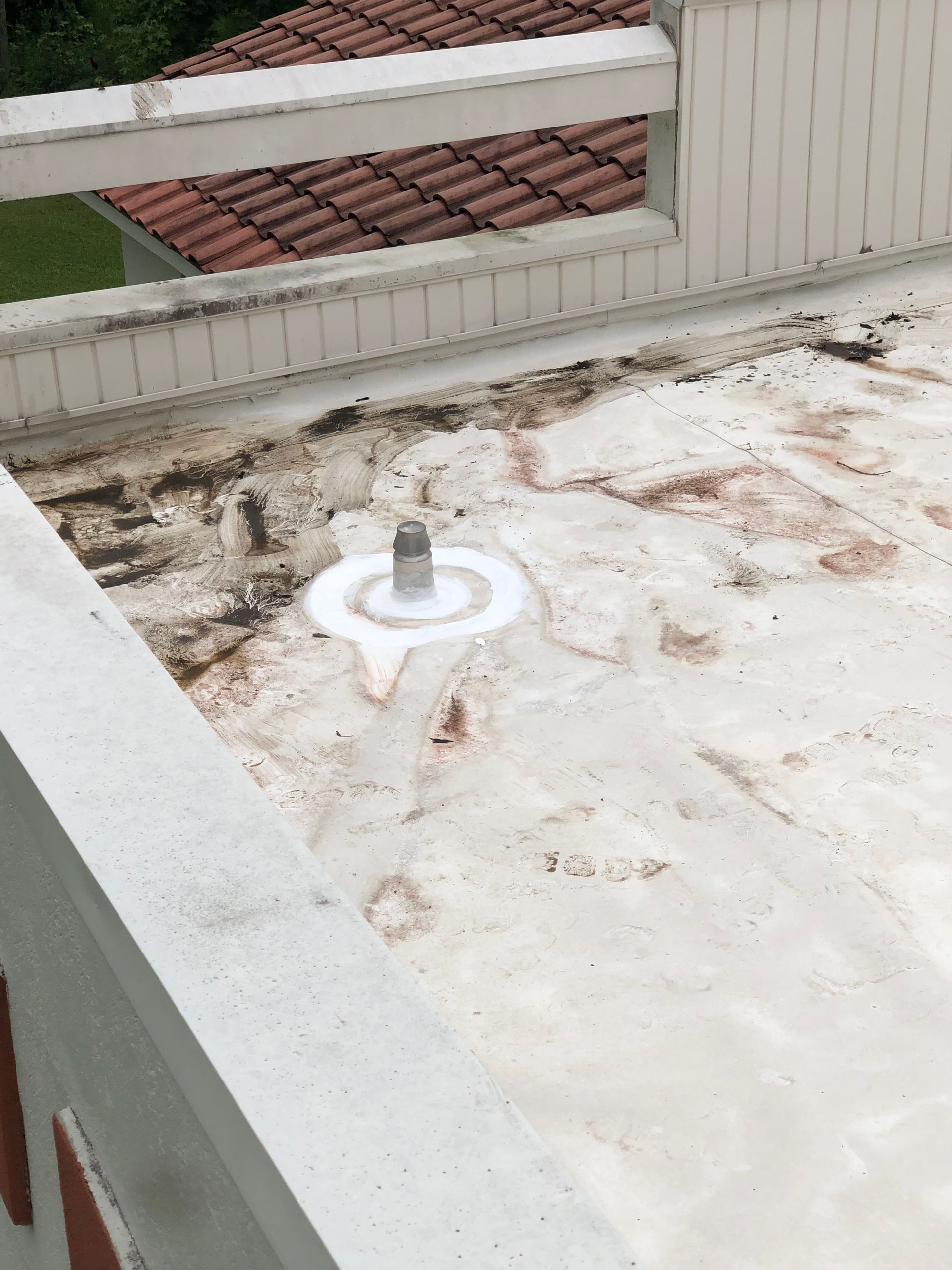White flat roof with a metal vent pipe and surrounding discoloration. A white railing is in the foreground.