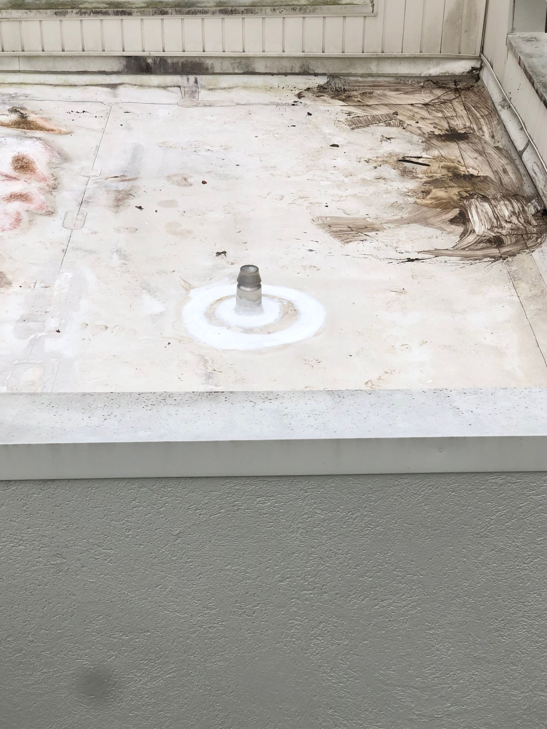 White roof with a metal vent pipe and staining. Concrete below.